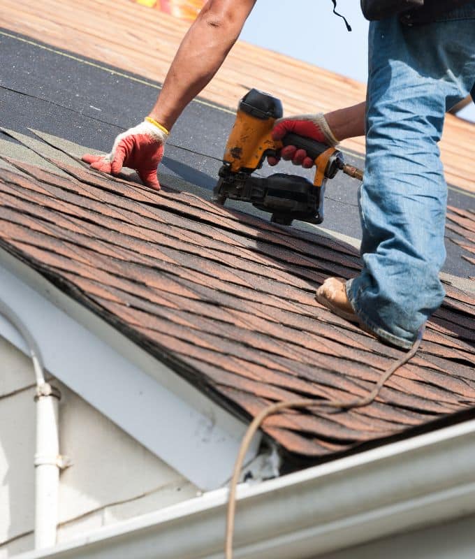 Roofing professional installing asphalt shingles with a nail gun on a residential roof.