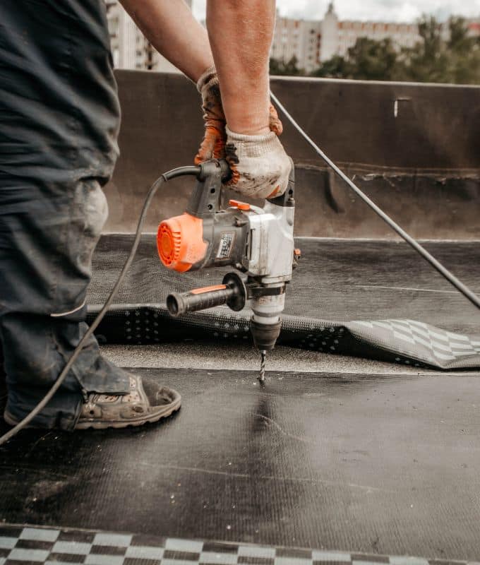 Close-up of a roofing professional securing a membrane layer with a power drill on a flat roof surface.