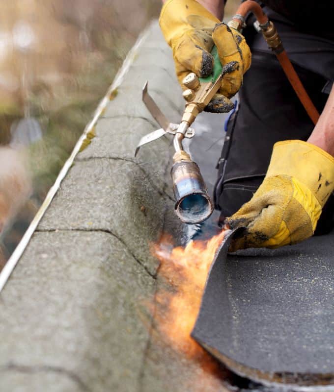 Roofing professional using a torch to apply heat for a seamless membrane installation on a flat roof.