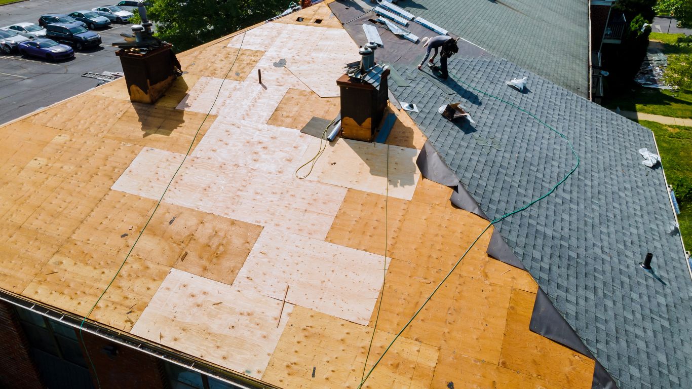 Commercial roof being replaced, with new shingles installed over wooden decking. Learn about Roof Replacement Cost for durable, long-lasting roofing solutions.